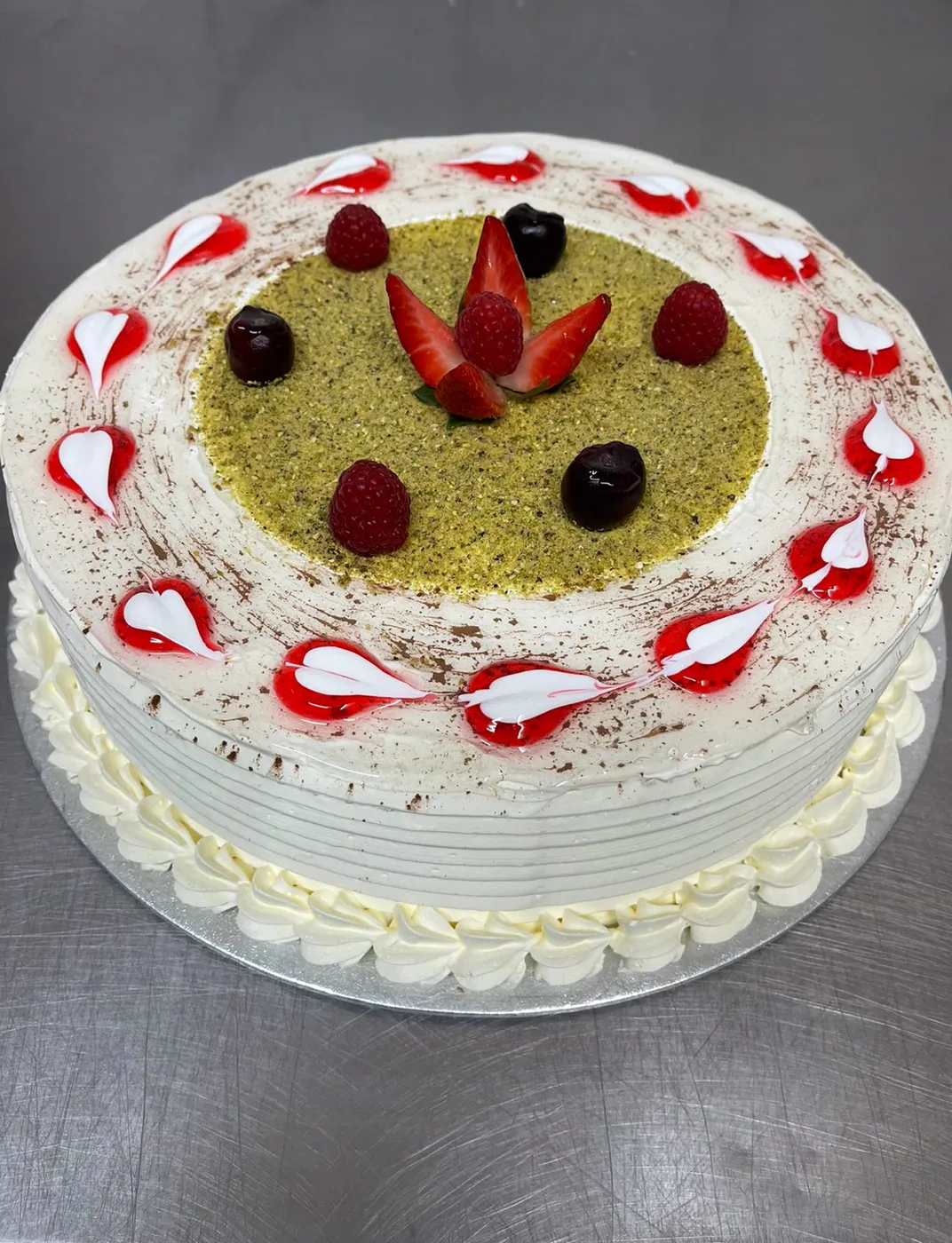 Round pistachio cake with cream piping, strawberries and berries