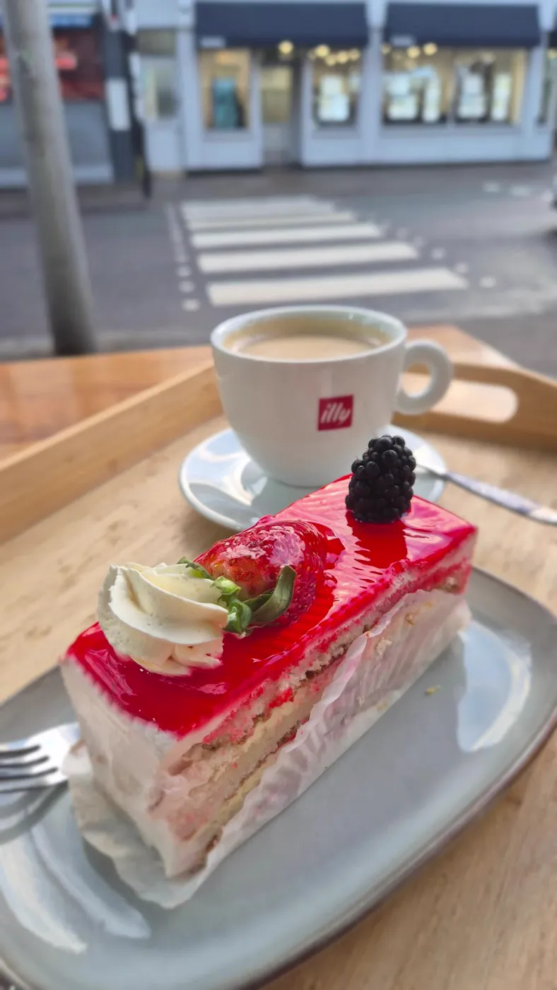 Coffee in a white cup beside a slice of strawberry cake